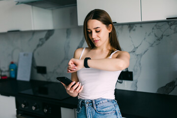 Fototapeta na wymiar Young woman tooking at her wrist watch while sitting on a table in a kitchen