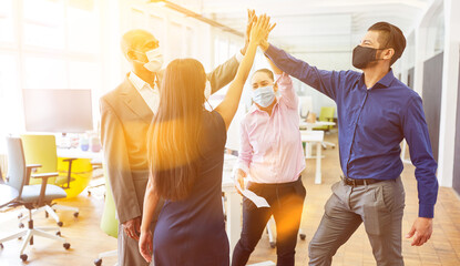 Business Team mit Mundschutz bei High Five im Büro