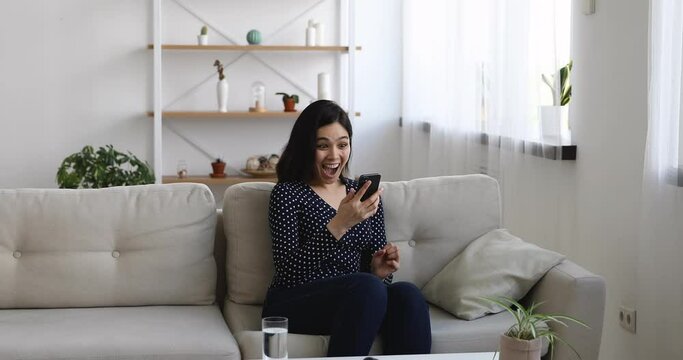 Vietnamese woman sit on sofa in living room hold smartphone received message stand up jumping feels excited looking very happy, opportunity new job of dream, got hired. Winner enjoy moment of victory