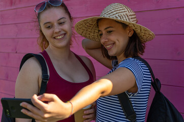 two young girls taking a selfie together on a pink background