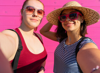 two young girls taking a selfie together on a pink background