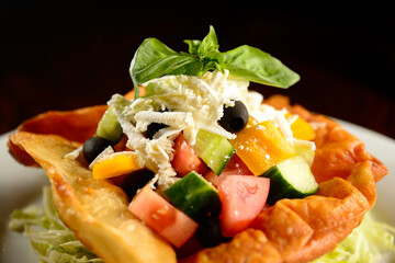 Mixed salad of tomatoes, peppers, olives, basil and cheese in fried tortilla on white plate