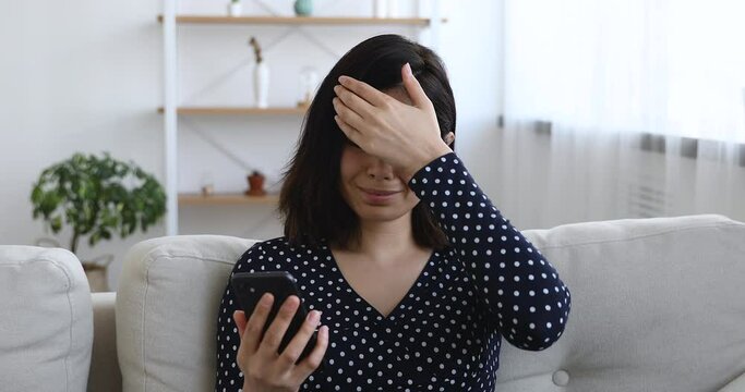 Asian woman sit on sofa hold cellphone read unpleasant news bad sms feels upset start crying. Bank notice about debt, student unsuccessful exam pass, not hired of dream job. Moment of failure concept