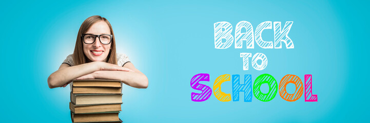 Young girl in a white dress and glasses put her hands on a stack of books on a blue background.