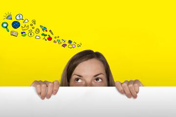 Girl Looks out from behind the White Paper Sheet on the Yellow Background. Added Icons in Wish Desires. Dream Girl Concept. - obrazy, fototapety, plakaty