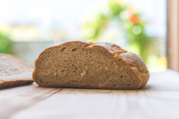 Fresh rustic bread in slices on wooden cutting board. Blurry background.