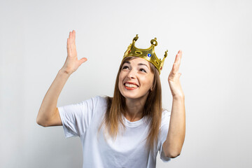 Young woman with a crown on her head emotionally rejoices and celebrates on a light background....
