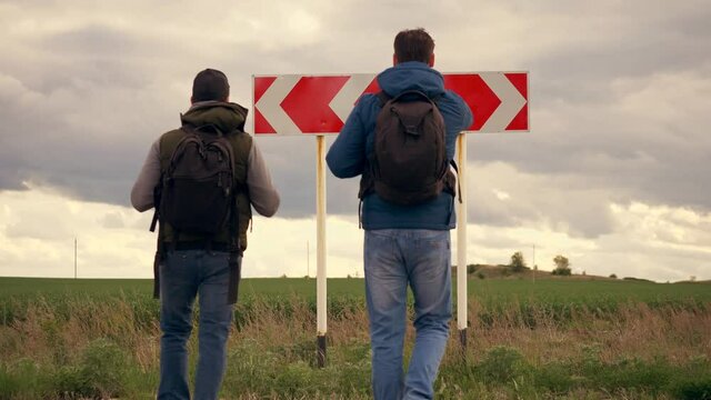 Teamwork. People are tourists, businessmen with backpacks approach the road sign of the direction of the road and choose the path. The problem of choice, decision making. Business travel concept.