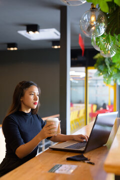 Young beautiful Asian businesswoman using laptop and sitting with distance inside the coffee shop