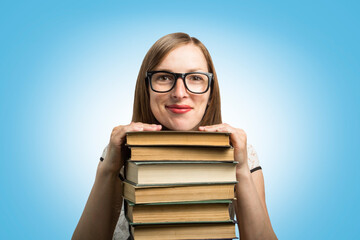 A young girl in a white dress and glasses put her hands on a stack of books on a blue background. Concept of a young student and education