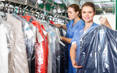 Fototapeta na wymiar Confident woman worker of dry cleaner showing clean clothes in plastic garment bag