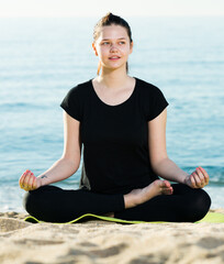 Fototapeta na wymiar Female 20-30 years old is sitting and doing meditation in black T-shirt