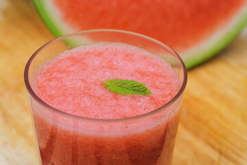 Summer watermelon juice inside of a glass of water with a watermelon slice on the background. Close up view.