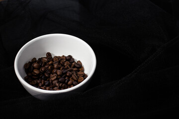 Coffee beans in a white сup on a black background. The view from the top.