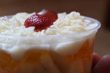 fresh fruit salad of melon, grape, strawberry, kiwi dressed with yoghurt  chopped Apple. cheese and fruits for upper topping. served in a square plastic on wooden tray. selective focus