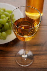 Glass of white wine in focus, Cluster of fresh grapes on a white plate and bottle of wine out of focus. Dark wood talbe surface.