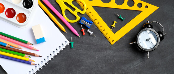 Back to school banner template. Flat lay colorful school supplies on black board background. Top view, overhead.