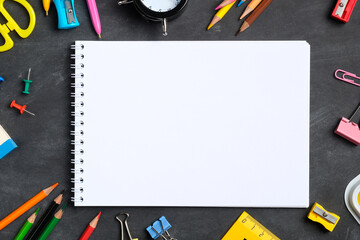 Blank paper notebook mockup and school supplies on black board. Flat lay, top view. Back to school concept.