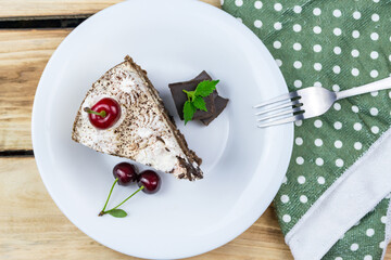A triangular piece of tiramisu on a white plate, a piece of chocolate, a cherry.