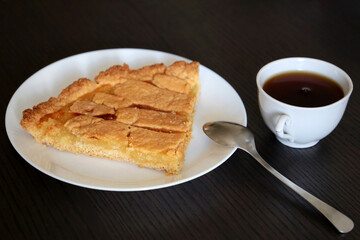 Lemon pie on white plate, cup of coffee and spoon on a wooden table. Concept of morning breakfast, sweet dessert and calories food