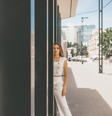 Fototapeta na wymiar A beautiful white girl posing in the background of a city building. The girl is dressed in a white suit. She has gorgeous hair and makeup. High quality photo