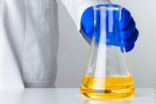 Scientist Or Doctor In Blue Gloves Pouring Some Yellow Liquid Into A Flask