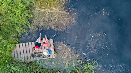 Happy family and friends fishing together outdoors near lake in summer, aerial top view from above
