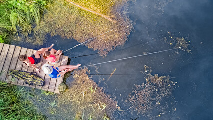 Happy family and friends fishing together outdoors near lake in summer, aerial top view from above

