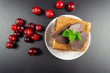Square piece of tiramisu on a white plate, decorated with chocolate.