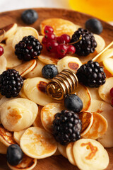 Tiny pancakes with berries, honey close-up on a wooden plate. Pancake cereal. concept of Breakfast, food trends.