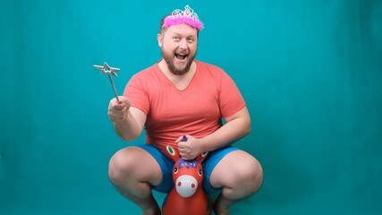 cute bearded freaky man in a pink T-shirt with a diadem on his head dreams of riding a unicorn with a magic wand in his hand. A funny wizard joke to make and fulfill a wish