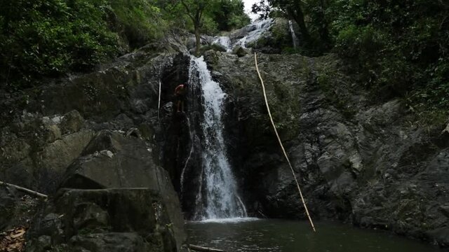 Man jumping off the edge of a cliff into a water fall in Tobago.