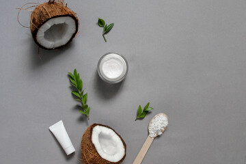 Fototapeta na wymiar Homemade coconut oil cosmetics for skin and hair care. Oil in small bottle, face cream, halves of coconut with shelf on grey background, top view copy space
