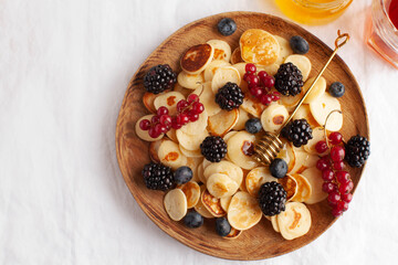 Tiny pancakes with berries and honey on a wooden plate. concept of Breakfast trends in the supply. Copy space