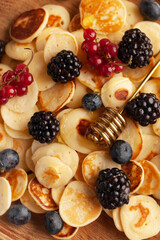Tiny pancakes with berries, honey close-up on a wooden plate. Pancake cereal. concept of Breakfast, food trends.