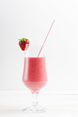 Strawberry and banana smoothie in a transparent glass on white wooden table. Copyspace.