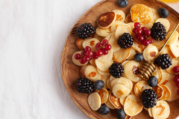Tiny pancakes with berries and honey on a wooden plate. concept of Breakfast trends in the supply. Copy space