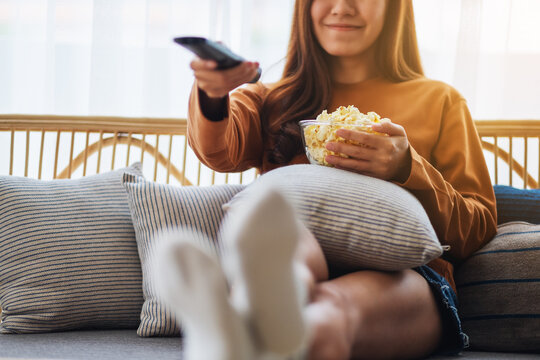 Closeup image of a woman eating pop corn and searching channel with remote control to watch tv while sitting on sofa at home