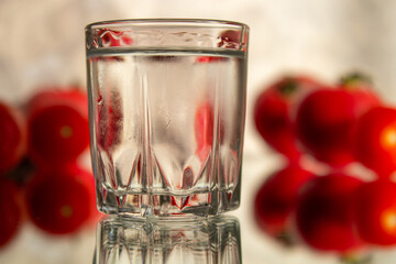 A glass of vodka in a glass on a mirror surface with tomatoes.