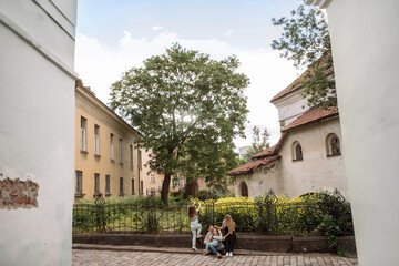 A young family with their daughters walks through the streets of Provence. There are yellow wildflowers, blooming trees, an old house and paving stones on the street. A girl climbs the fence. Father h