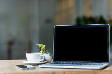 Mockup of laptop computer with empty screen with coffee cup and smartphone on table of the coffee shop background,black screen