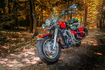 Fototapeta na wymiar Red Road Bike Cruiser. Motorcycle cruiser stands on dirt road in sunny autumn forest. Walk ride on chopper in forest road