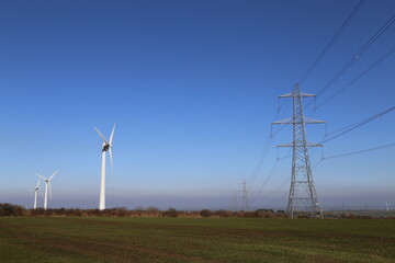 Fototapeta na wymiar Wind turbines sited beside high-voltage electricity pylons on a hilltop in Devon, England.