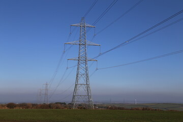 High-voltage electricity pylons overlooking farmland on a hilltop in Devon.