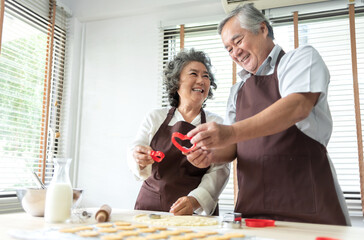 Senior couple smiling holding cookie cutter in heart shape baking in kitchen