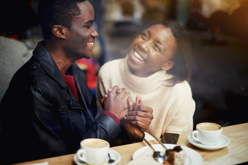 View through window of cheerful happy lovers enjoying leisure while sitting in bar in cold winter day, young black man and woman with beautiful smiles on faces having fun during rest in coffee shop