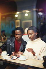 Two young friends having joint lunch in restaurant during work break, students relaxing in cafe after lectures in University, beautiful black couple get warm in coffee shop after strolling in cold day