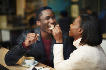 Beautiful dark skinned couple in love having a great time together, man and woman enjoying each other, young woman feeding man with dessert cake at their dating