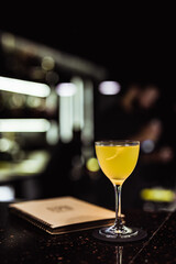 A sour cocktail in a nick and nora glass in a dark and moody atmosphere of a bar