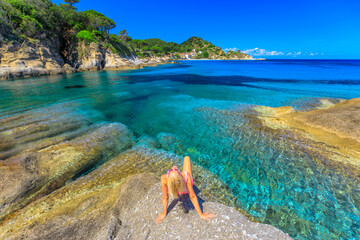 Woman in pink swim suit resting and sunbathing in Cotoncello Beach near popular Sant 'Andrea beach,...